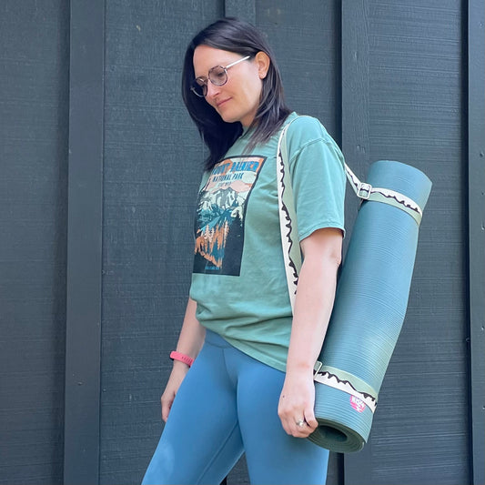 Woman holding a yoga mat with a strap against a dark wall