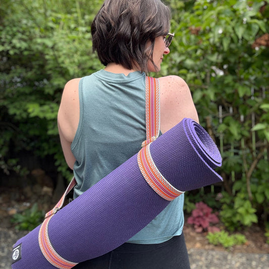 Person holding a purple yoga mat with straps outdoors