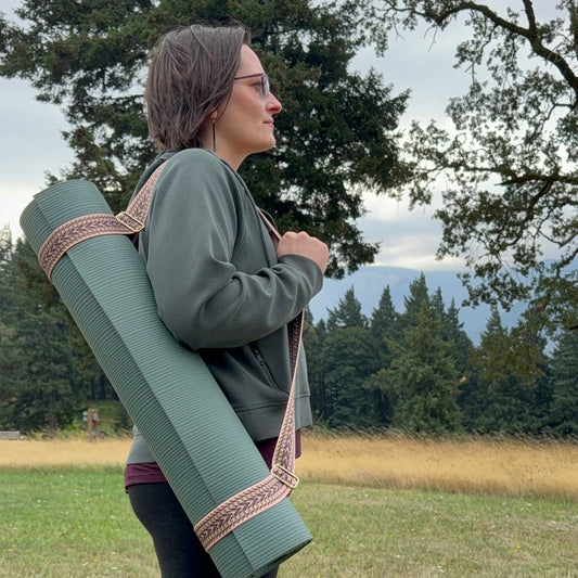 Person holding a yoga mat outdoors in a natural setting with trees and mountains.