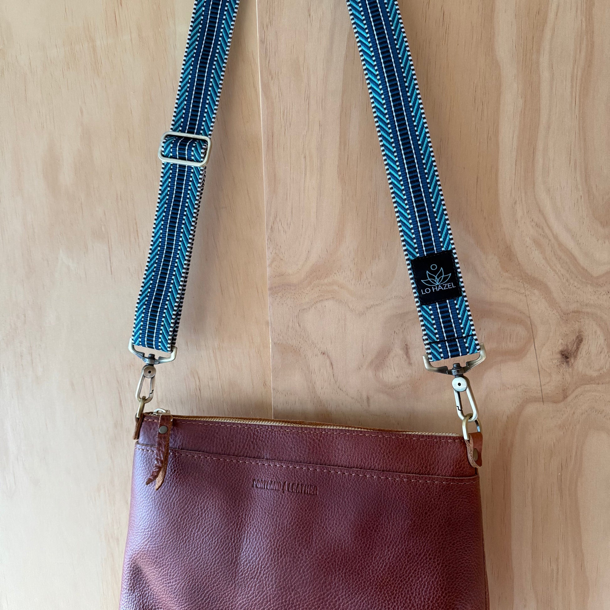 Brown leather purse with blue strap on a wooden surface