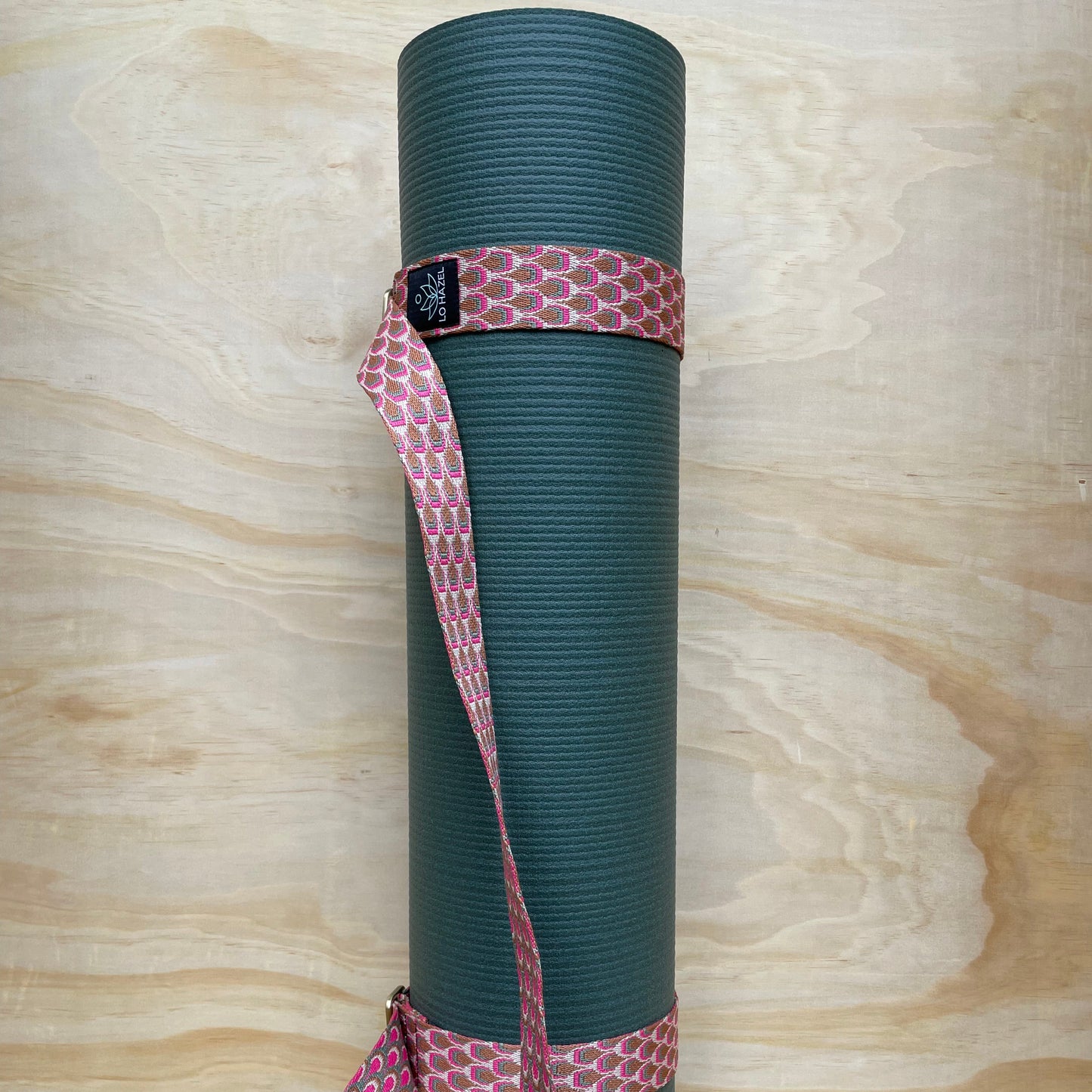 Green yoga mat with a pink strap on a wooden surface