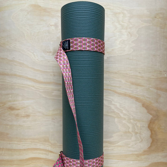 Green yoga mat with a pink strap on a wooden surface