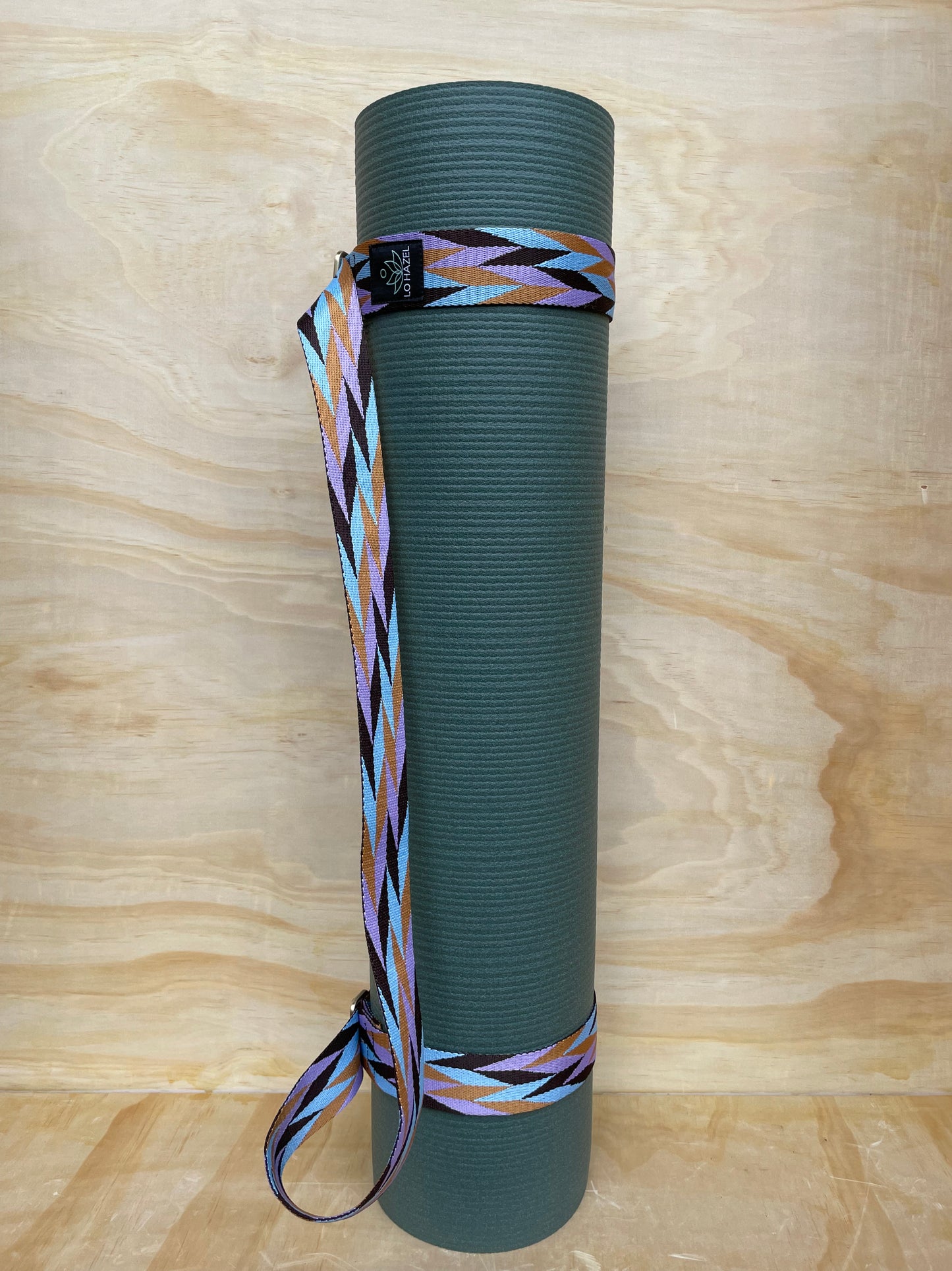 Green yoga mat with a colorful strap on a wooden surface