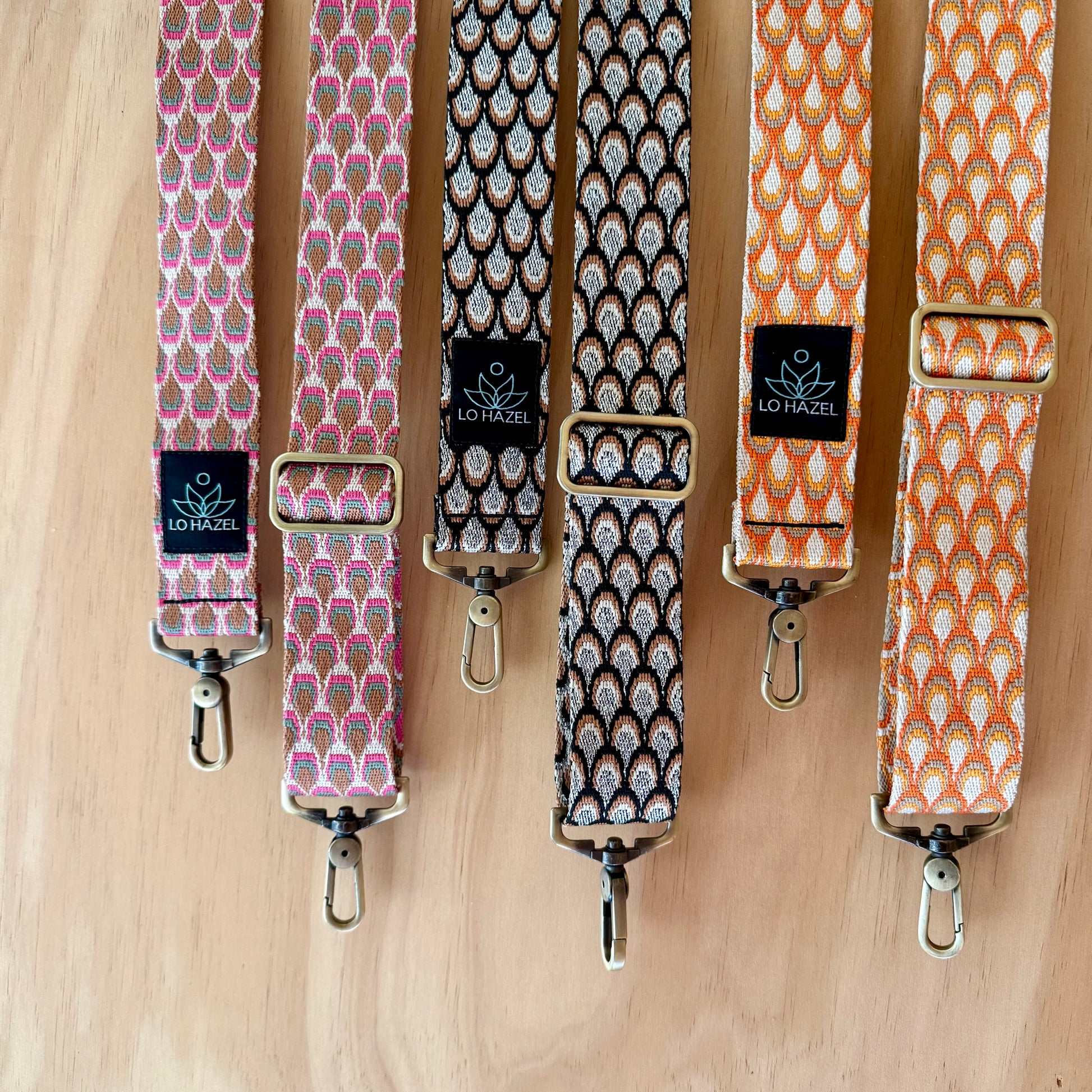Four patterned bag straps with metal buckles on a wooden surface, featuring the brand 'LO HAZEL'.